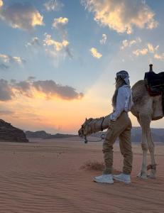 a person standing next to a camel in the desert at Sand Rose Camp - Wadi Rum in Wadi Rum