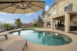 a swimming pool with an umbrella next to a house at Heated Pool 3BR Retreat Estrella Mountain in Goodyear +25 photos