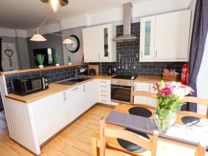 a kitchen with white cabinets and a table with a vase of flowers at Corvette in Trearddur