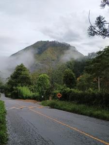 a road with a mountain in the distance with clouds at Hospedagem do Rio in Nova Friburgo