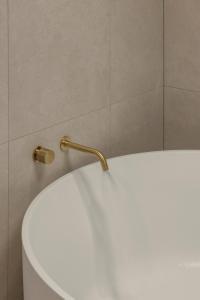 a white toilet with a gold faucet on top of it at Little Waves Tugun in Gold Coast +14 photos