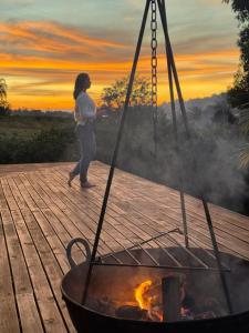 a woman walking on a deck with a fire pit at Chalé romântico com jacuzzi e vista do pôr-do-sol in Harmonia