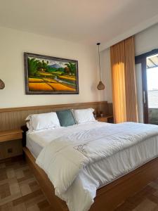 a bedroom with a large white bed with a painting on the wall at Holi Saren Guest House in Nusa Dua