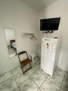 a room with a refrigerator and a tv on a wall at Dina Suítes Flat's Caiçara in São Sebastião