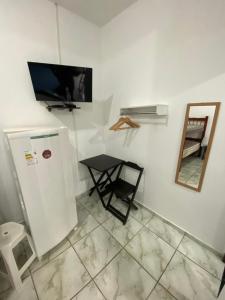 a room with a tv and a table and a mirror at Dina Suítes Flat's Caiçara in São Sebastião