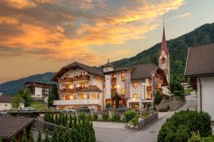 a building in a village with a church at MyLiving - Hotel B&B by Majestic Resorts Dolomites in San Lorenzo di Sebato