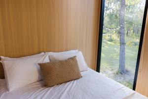a bed with a pillow in a room with a window at Wilderness Whisper 1770 By Tiny Away in Agnes Water