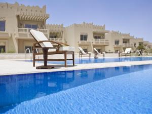 a hotel swimming pool with chairs in front of a building at Grand Hyatt Doha Hotel & Villas in Doha