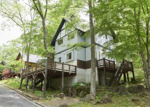 a large white house with a deck in the woods at 森のRetreat -foresta di luce- in Hatsukaichi