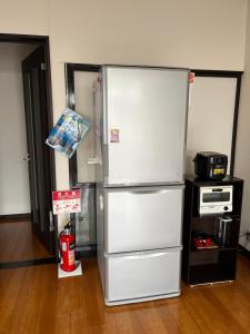 a white refrigerator in a kitchen with a fire extinguisher at 民泊 シェアハウス北浦 in Senboku