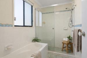 a white bathroom with a tub and a window at Hawks Nest Hideaway | Spa, BBQ, Bikes & Pool Table in Hawks Nest +29 photos