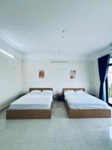 two beds in a white bedroom with a window at Tie Homestay in Dong Hoi