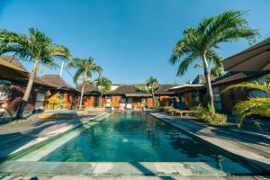 a swimming pool in front of a house with palm trees at Turtle Villas, Canggu by Manara in Canggu