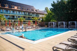 a large swimming pool with people sitting in chairs in front of a hotel at Wellness Hotel Gyula in Gyula