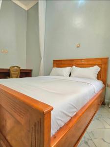 a bedroom with a wooden bed with white sheets at Gibson Motel in Mbarara