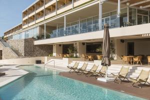 a swimming pool with chairs and an umbrella next to a building at Divani Corfu Palace in Corfu