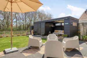 a backyard patio with white chairs and an umbrella at Groenendijk Verhuur Vakantiewoning Casa Iris in Burgh Haamstede