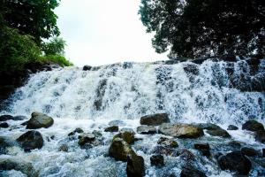 a waterfall with rocks in front of a river at Harmony Hills Ecostay in Nasrāpur +10 photos