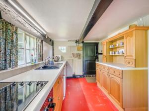 a kitchen with wooden cabinets and a red floor at Glebe Cottage in Powick
