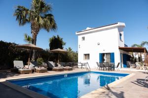 a pool with chairs and umbrellas next to a house at Dream Olea Villa - Ayia Napa in Ayia Napa