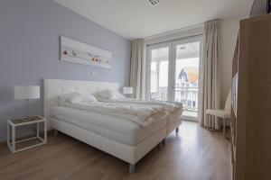 a white bedroom with a bed and a large window at Duinhof IX E204 in Cadzand