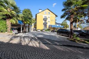 a street with a yellow house and palm trees at Hotel Nikolasch mit eigenem Seebad - Adults Preferred in Millstatt
