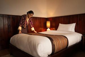 a woman standing next to a bed in a hotel room at Yangkhil Resort in Tongsa
