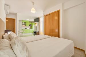 a bedroom with a large white bed and a kitchen at Apartamentos Mirante da Rocha in Portimão