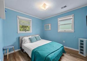 a blue bedroom with a bed and two windows at Central OBX Getaway with Pool and Sound Access in Nags Head