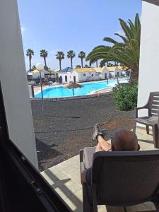 a man sitting in a chair looking at a swimming pool at First Love in Caleta De Fuste