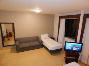 a bedroom with a bed and a couch and a television at Prinz Apart Hotel in Joinville