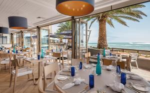 a restaurant with tables and chairs with the ocean in the background at Strand Hotel Swakopmund in Swakopmund