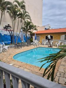 a swimming pool with palm trees and a building at Pousada Casa Da Arara suíte 104 in Saquarema