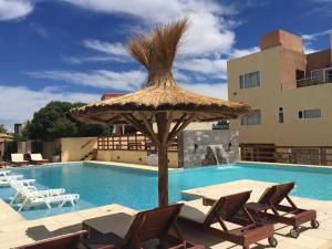 a table and chairs with a straw umbrella next to a swimming pool at Complejo Tamariscos in Las Grutas