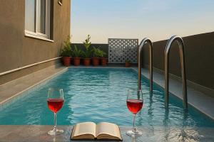 two glasses of wine and a book next to a swimming pool at Ellara Homes in Udaipur