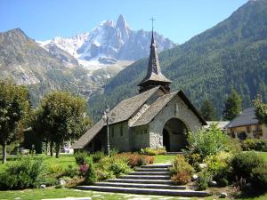a church with a steeple with mountains in the background at La Ferme des Praz apartment - Chamonix All Year in Chamonix