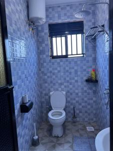 a blue tiled bathroom with a toilet and a window at Elp Living in Hoima