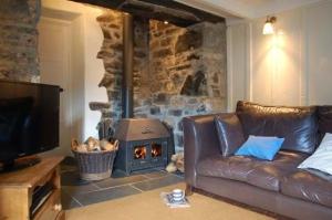 a living room with a leather couch and a wood stove at Pebbles in Cadgwith