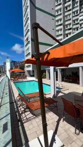 a patio with an umbrella and chairs and a swimming pool at Hotel Sete Coqueiros in Maceió