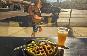 a woman walking past a table with a plate of food and a drink at Mountain Star Inn Cedar City in Cedar City