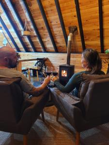 a man and a woman sitting in chairs in front of a stove at Chalé Encanto Do Lago in Urubici
