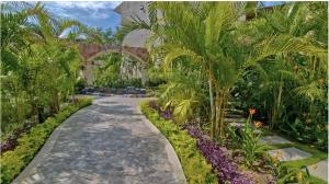 a path through a garden with palm trees and purple flowers at Escape to Paradise in Tangolunda