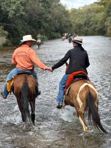 two people riding horses through a river holding hands at Pousada Chalés do Rancho Canastra in Vargem Bonita