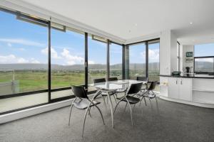 a dining room with a table and chairs and large windows at U Suites at The Links in Paraparaumu