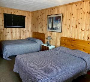two beds in a room with wooden walls at Chicken Shack Motel in Batchawana