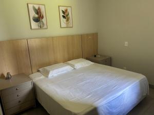 a bedroom with a white bed with two nightstands and two pictures at Apartamento confortável, calmo e bem localizado in Lucas do Rio Verde