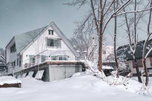 a white house with snow on the ground at Hakuba Slopeside Chalet in Otari