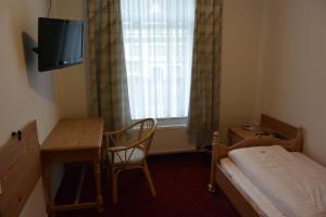 Habitación pequeña con cama, escritorio y TV. en Hotel Deutsches Haus en Blomberg