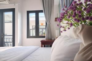 a bedroom with a bed with a vase of purple flowers at ICHI Home Kim Long in Hue