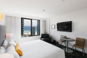 a white hotel room with a bed and a tv at voco Gold Coast by IHG in Gold Coast